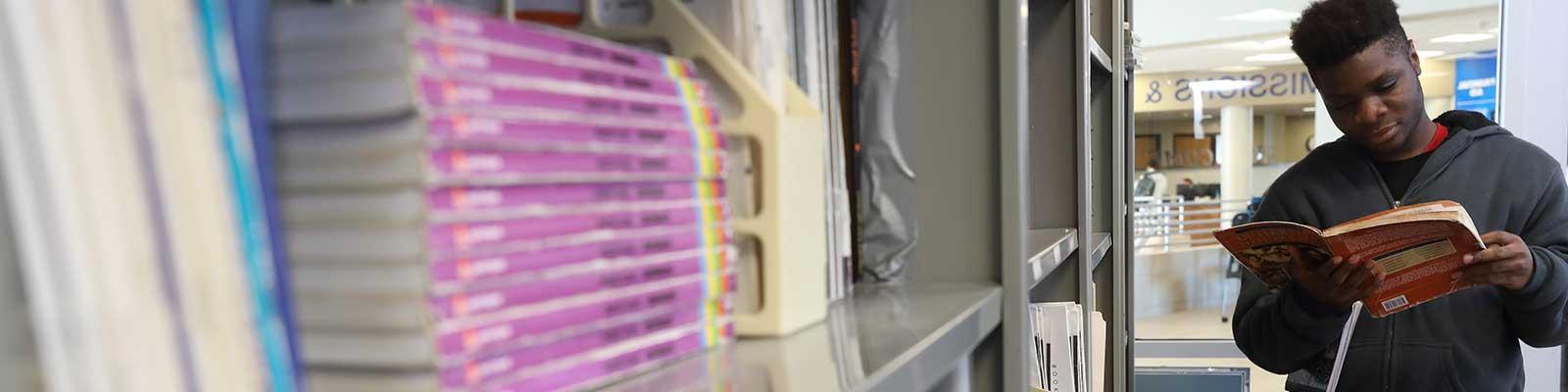 Student reads a book near a bookshelf